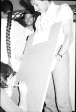 A student signing on a board titled “In Memory..” and “Mardi Gras ‘83”