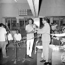 The judge of an event, possibly a quiz, handing over a trophy to a student