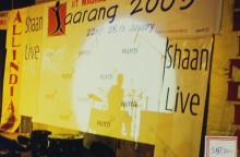 The shadow of a drummer falls on the screen behind the stage, 2003