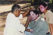 A student gets his face painted by an artist for a dramatics event (possibly)